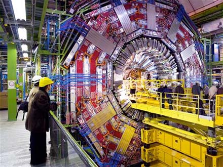 Engineers stand on a raised platform inserting the tracker into into the heart of the CMS detector. The detector looks enormous next to the people.
